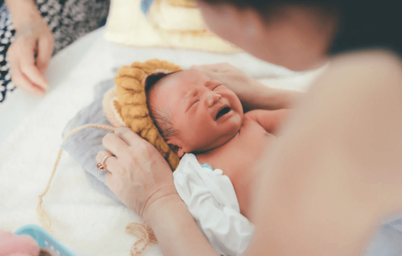 Newborn baby crying and being handed to mother